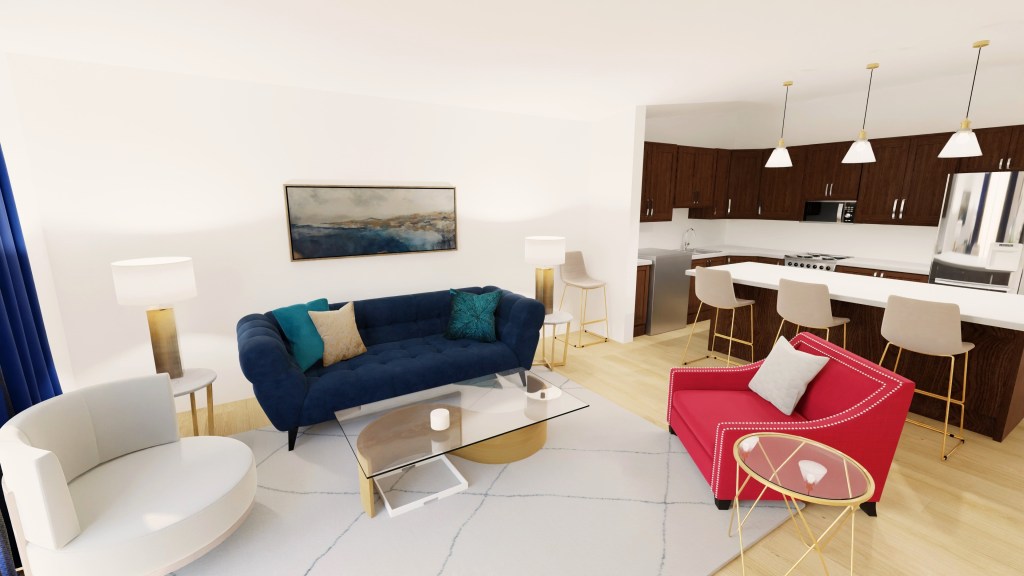 Standing in the corner where the office is, you turn and see the whole living space with the kitchen behind it. The deep navy couch has teal and gold pillows tossed across it and looks striking across from the pink chair.