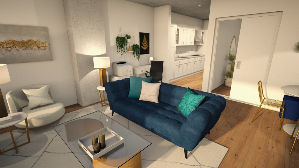 Looking from the windows into the living space, a large navy blue sofa that matches the ottomans in the adjacent dining space sits centrally in the room. It has been layered with teal throw pillows. A round white boucle chair sits across from it on the left. Each is paired with a round marble and gold end table with a statement gold lamp a top each. A gold coffee table sits centered in the space with a soft white rug expanding out underneath, defining the living space. From here you can see into the small office nook behind the couch on the left and beyond that to the kitchen.