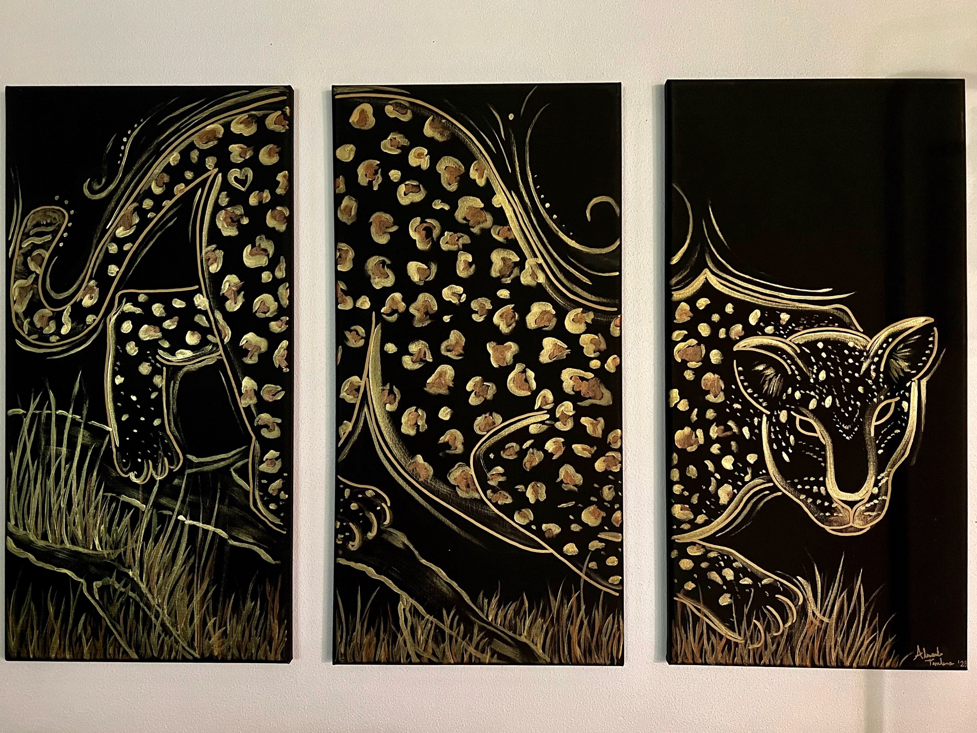 a three panel black triptych with a large golden abstract leopard climbing down a branch through the grass. It's spots done in gold and bronze, it's face geometrically decorated in a tribal style.
