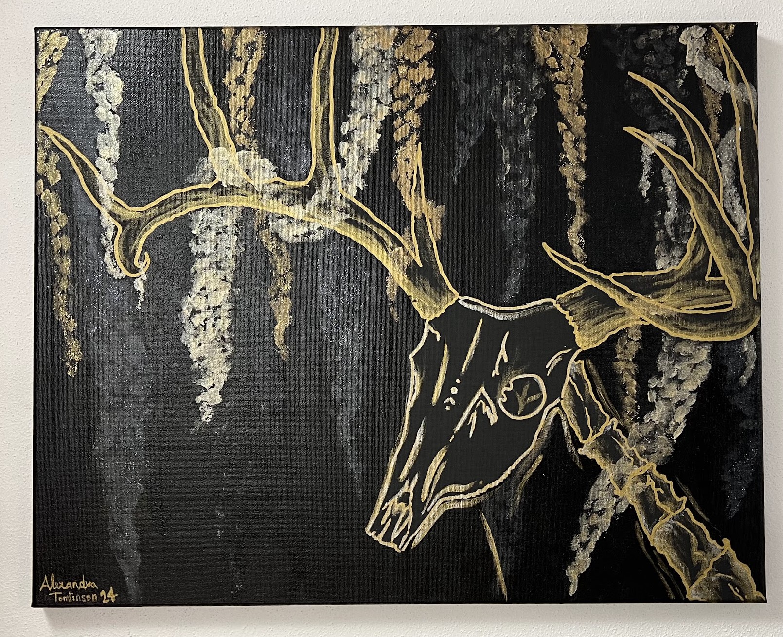 a black canvas with an off center skeletal deer peering it's head towards you. It's large antlers outstretch above where they intermingle with strands of gold, white gold, and black pieces of spanish moss.