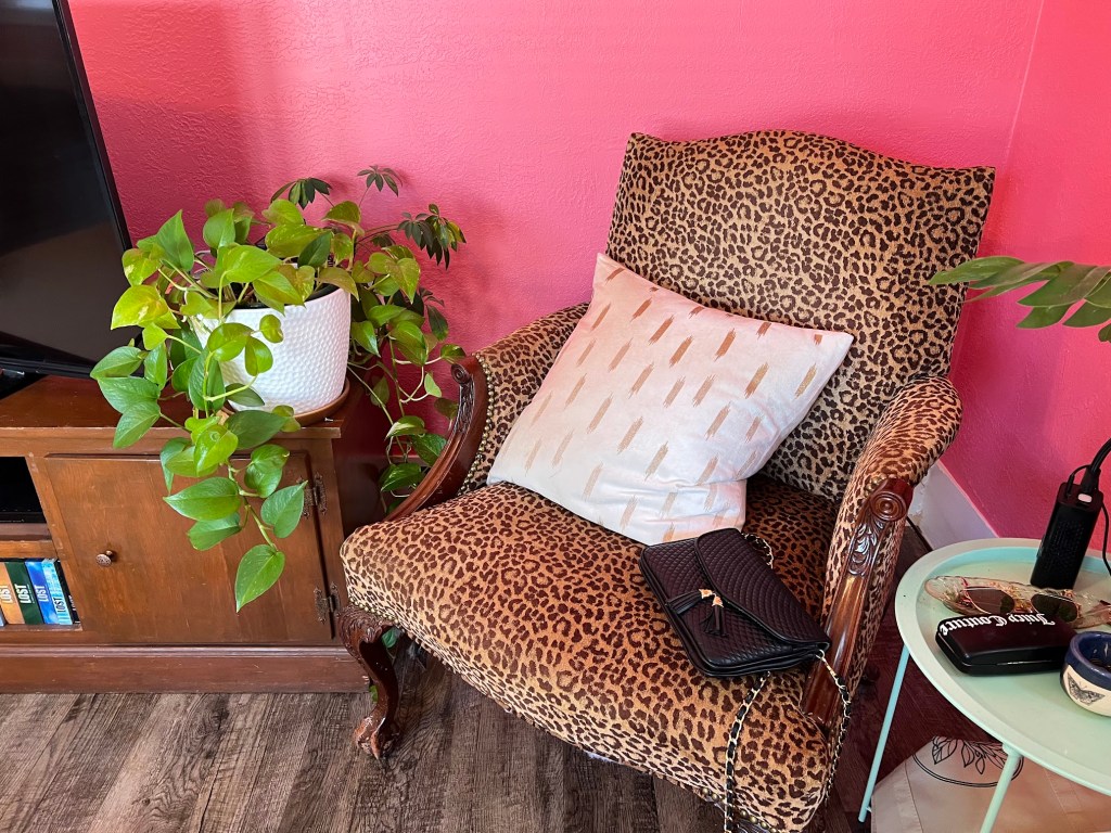 On the opposite side of the entry, a vintage queen anne chair done in leopard print sits next to a media cabinet. It's topped with a white and gold pillow and a black purse, with a large pothos on the adjacent cabinet.