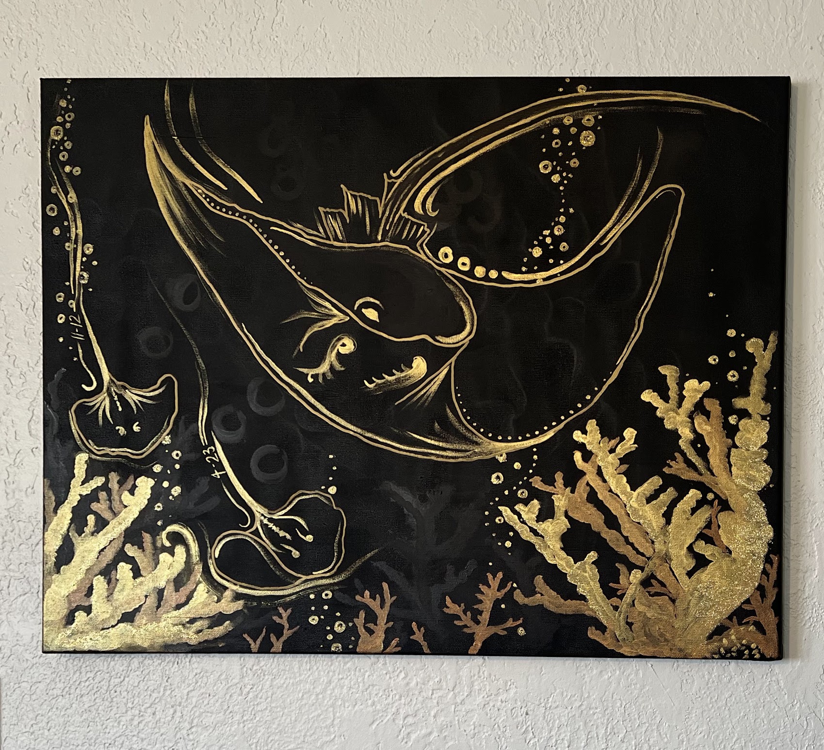 in my gold style, a giant stingray swoops down above a bed of coral, two smaller stingrays swim under the mother's fin, bubbles and swirls dancing around them where their birthdates are concealed. The coral below is bronze and gold, with some bubbles dotting the underwater scene.